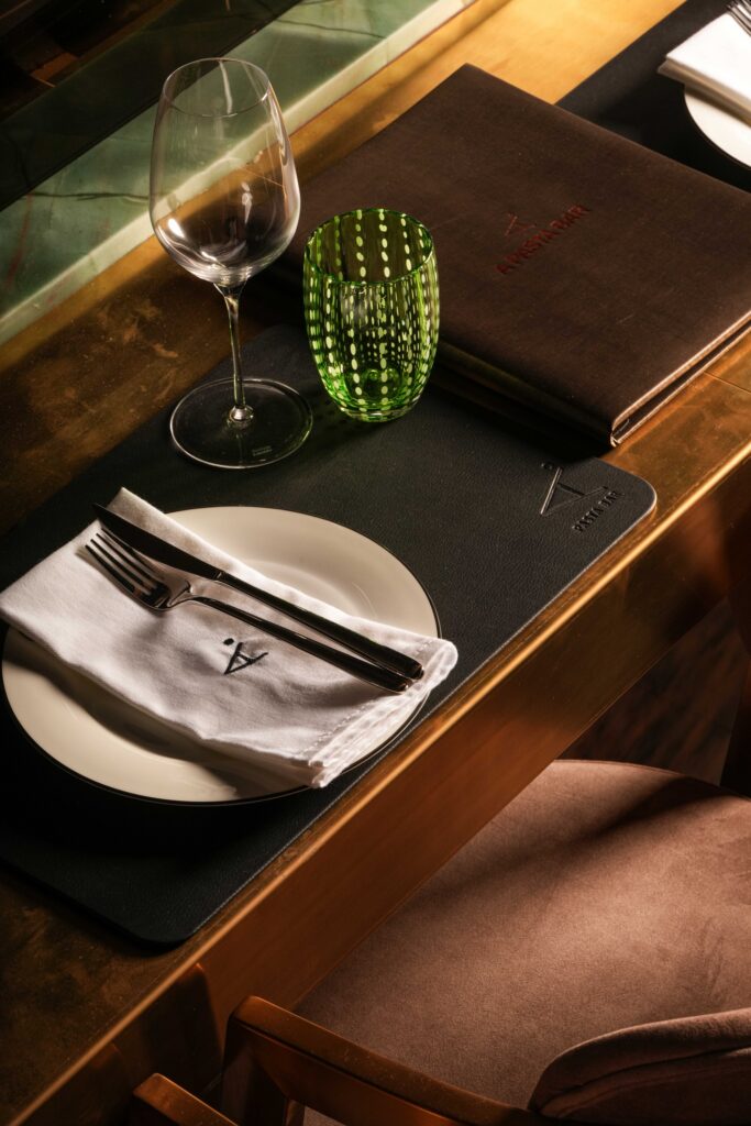Place setting with a white napkin, green tumbler, wine glass and brown menu.