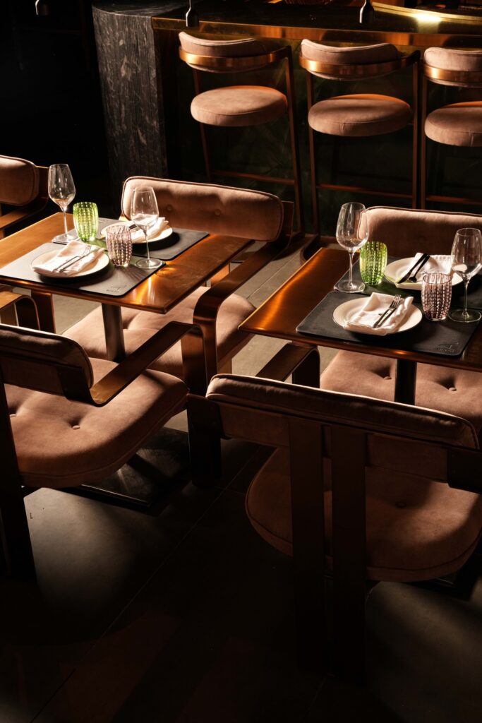Restaurant dining tables in warm sunlight with a row of bar stools behind them.
