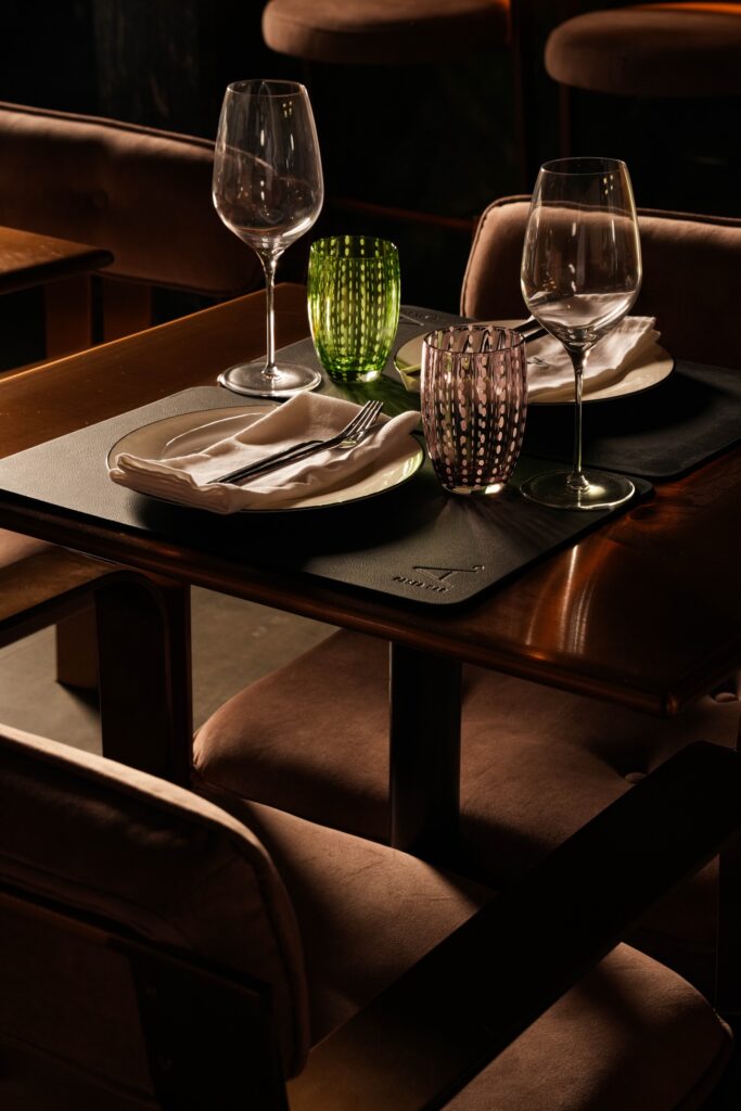 Close-up of a table for two with wine glasses and green and pink tumblers.