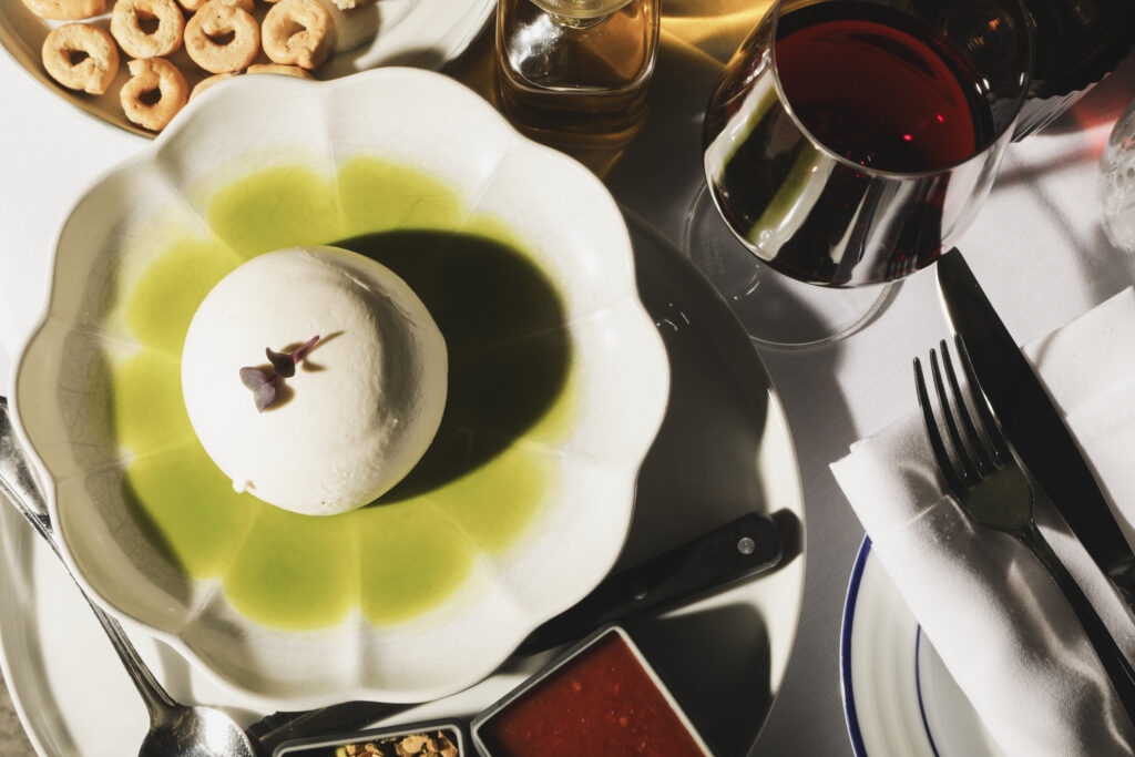 Soft white cheese in green herb oil, with red wine and bread rings on the table.