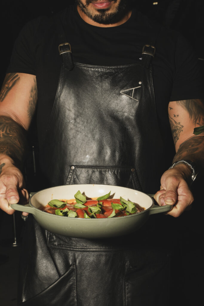 A member of staff wearing a black apron holds a bowl of mixed salad.