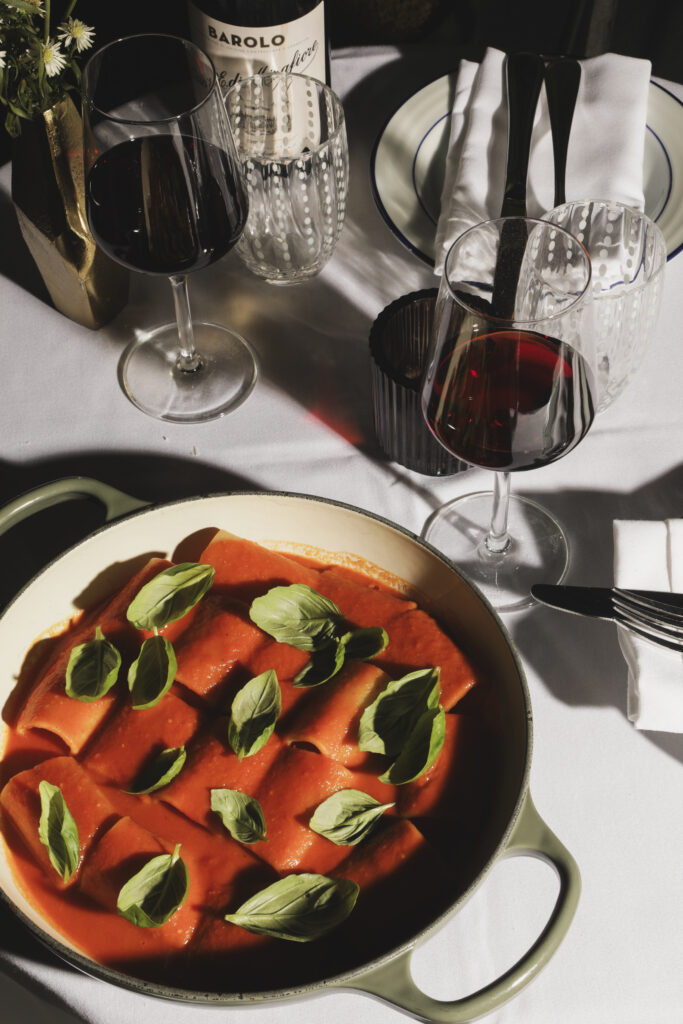 Pasta tubes in tomato sauce with fresh basil, served beside glasses of red wine.