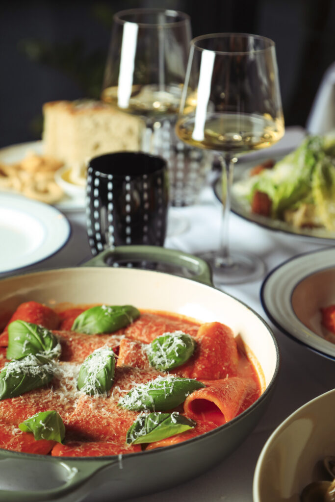 Pasta tubes in tomato sauce topped with basil and grated cheese, with white wine on the table.