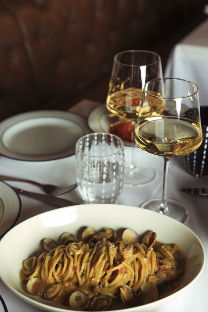 Spaghetti with clams served beside two glasses of white wine.