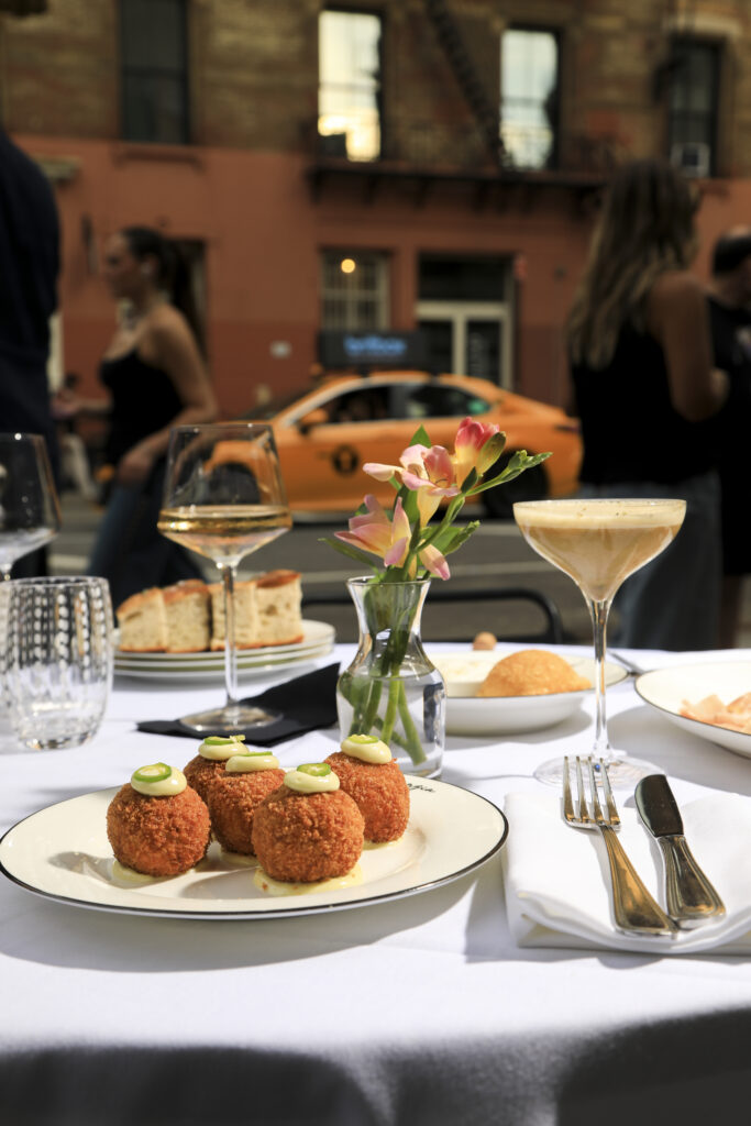 Fried croquettes and cocktails on a sunlit outdoor dining table.