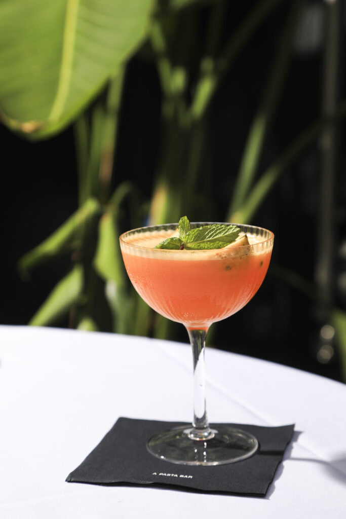 Pink cocktail in a coupe glass with a mint garnish.