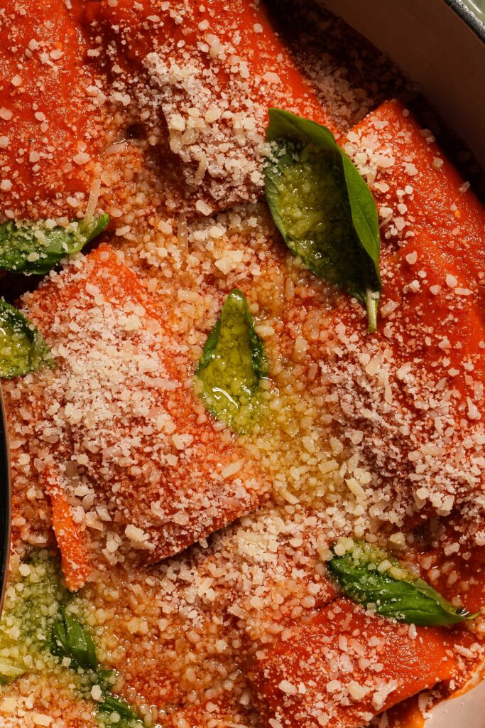 A close-up of pasta tubes in tomato sauce topped with grated cheese and basil.