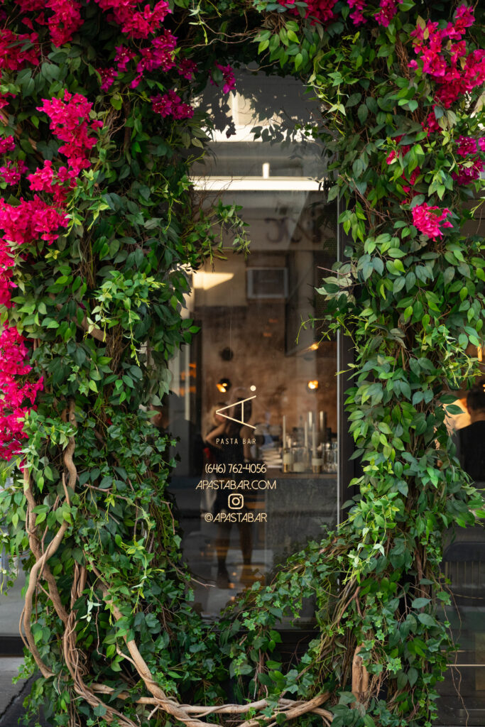 The restaurant window framed by green vines and pink flowers.