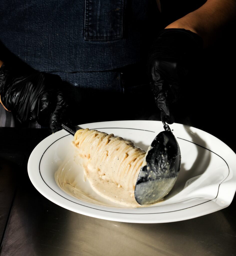 Cacio e pepe being arranged in a white bowl by gloved hands.