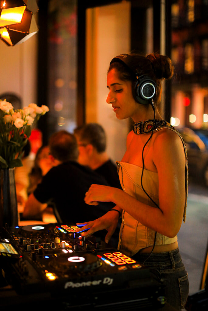 A DJ wearing headphones mixes music beside the restaurant's dining tables.