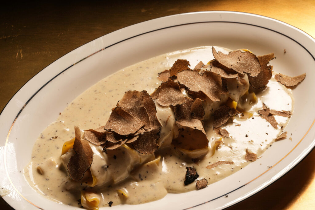Pasta in a creamy sauce topped with thin truffle shavings on an oval plate.