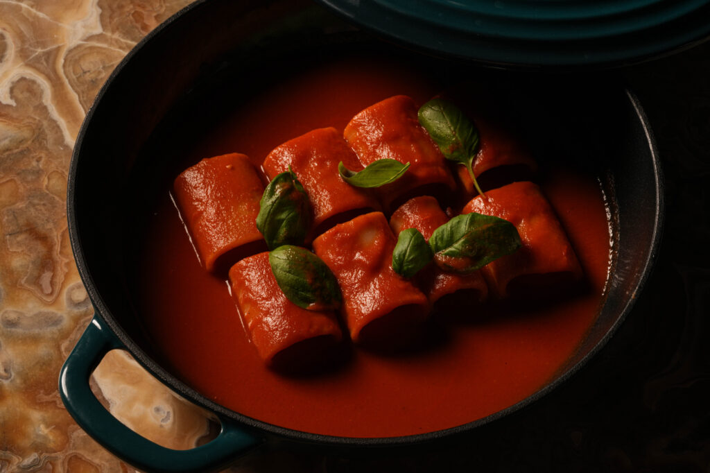 Large pasta tubes in tomato sauce topped with basil leaves in a black pan.