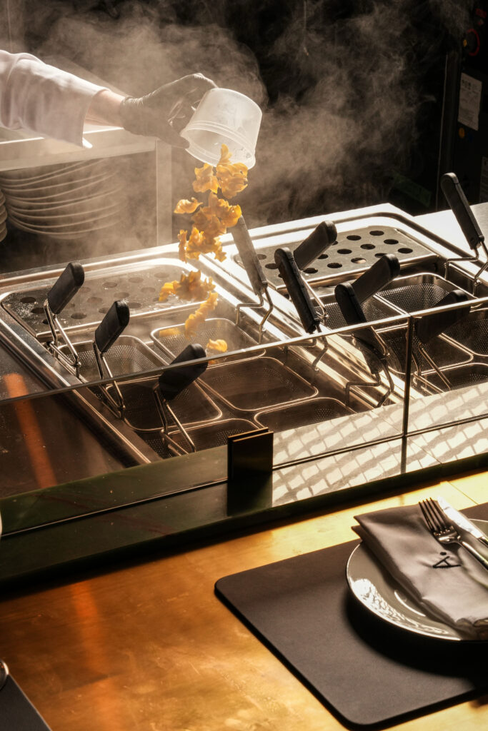 Chef tipping pasta from a container into a basket over steaming cooking water.