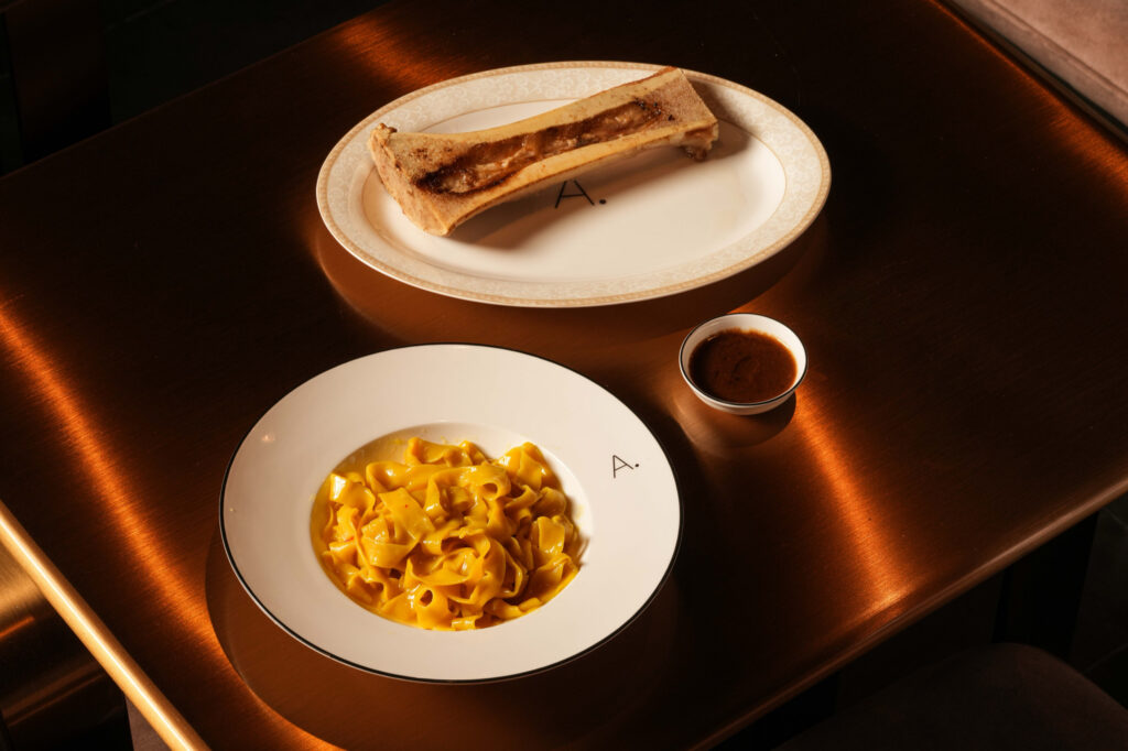 Ribbon pasta served with a roasted marrow bone and a small bowl of sauce.