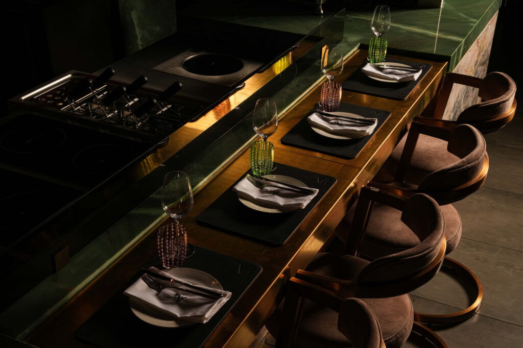 Place settings and colourful glasses along the kitchen counter beside upholstered stools.