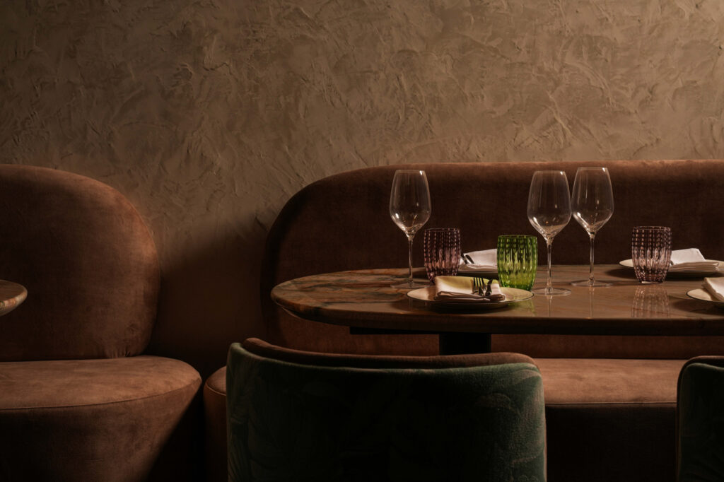 Curved dining booth with a marble table, green patterned chairs and colourful glassware.