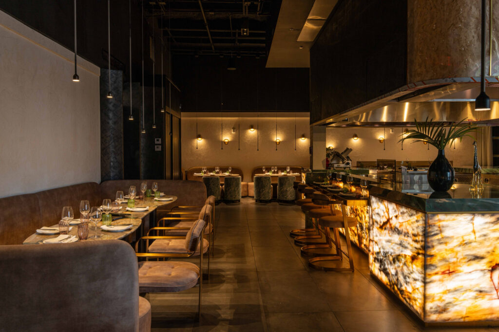 Dining room with curved banquette seating alongside an illuminated stone kitchen counter.