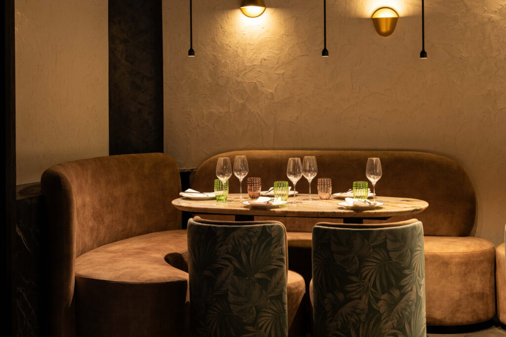 Marble table set for four in a curved booth with green patterned chairs.