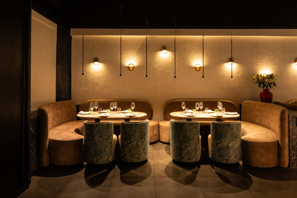 Two curved booths with marble dining tables and green patterned chairs beneath wall lights.