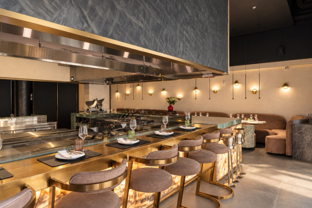 Counter seating around an open kitchen beneath a large extractor hood and pendant lights.